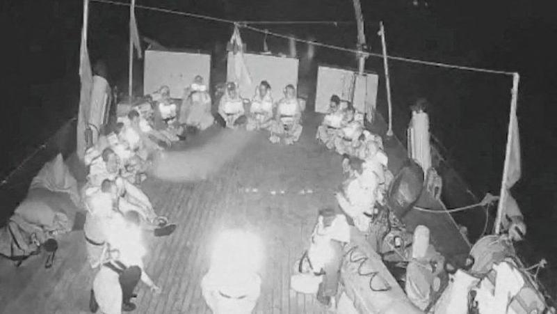 Black and white livestreamed footage shows crew members of the Alma vessel