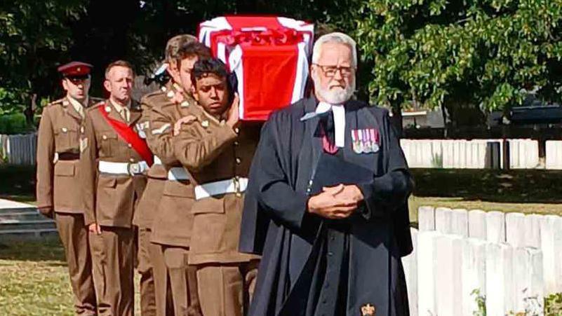 A coffin covered in a British flag being carried by soldiers.
