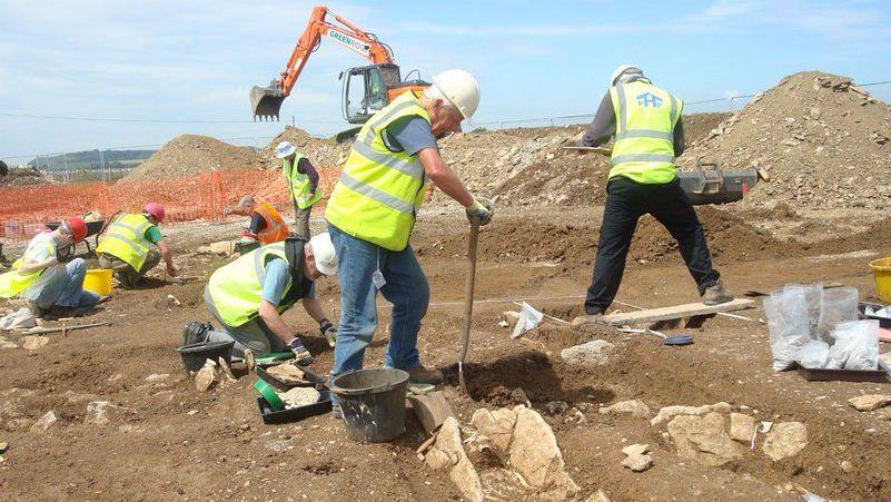 Men in high-vis vests digging up ground.