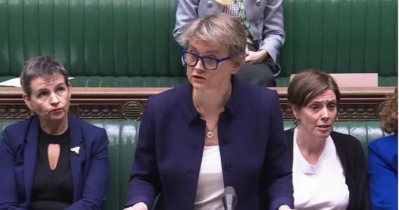 Home Secretary Yvette Cooper is delivering a speech at the dispatch box in the House of Commons. She is wearing glasses and a blue suit and other cabinet members are seated behind her on the green benches.