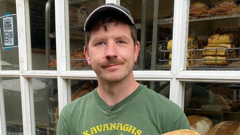 A man, who has short brown hair and a moustache, wearing a cap and a green t-shirt. 