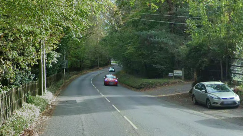 Cars travel along a road. Trees line either side of the carriageway.