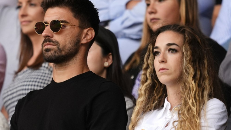 Jota's wife Rute has long drown dark hair and is wearing a white suit. Neves has sunglasses on and a black top. He has dark hair and beard.