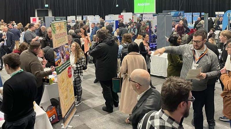 Crowds of people at the jobs fair around stands with job information printed on the and people sitting at desks