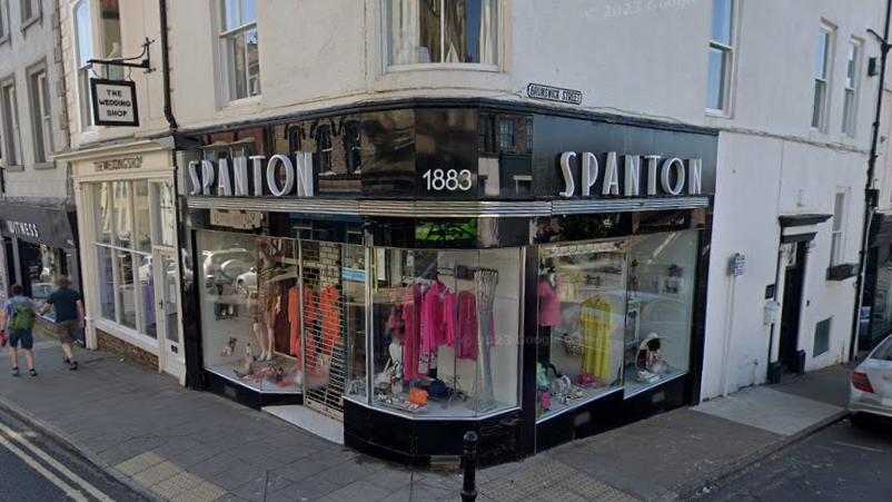 Spanton 1883 on a corner of a street. It has black and white art deco frontage and colourful women's clothes in the windows.