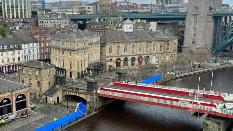 Blue flood barriers alongside the quayside with man in yellow jackets checking 