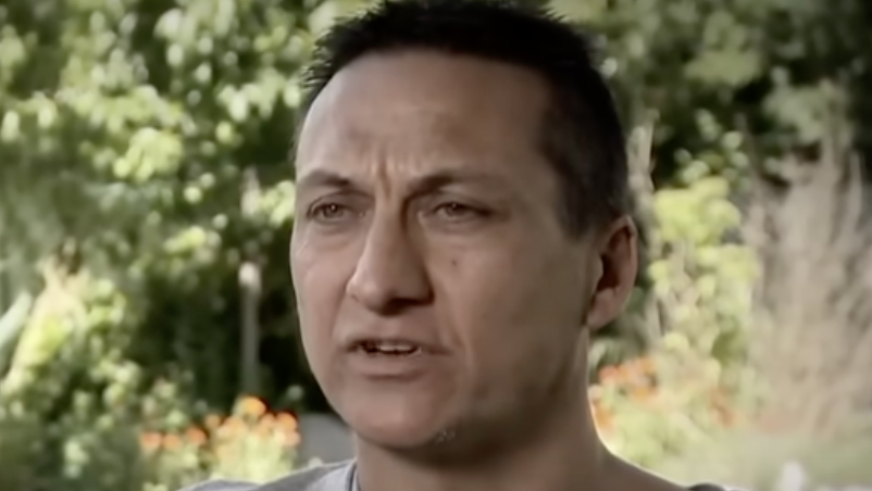 Dezi Freeman is photographed. He has dark hair and stands in front of a garden.
