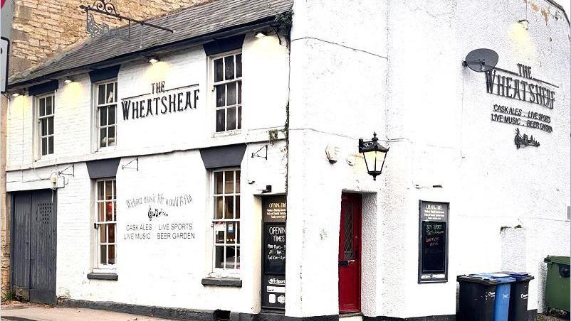 The exterior of the Wheatsheaf pub in Calne, Wiltshire, it is painted white with a large black door and the name of the pub written on the second floor.