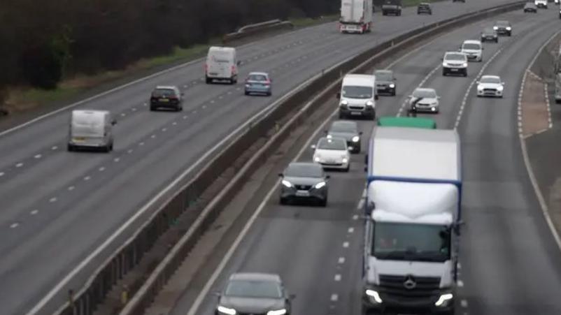 Cars driving on a dual carriageway on an A-road. There are a number of vans and a lorry too.