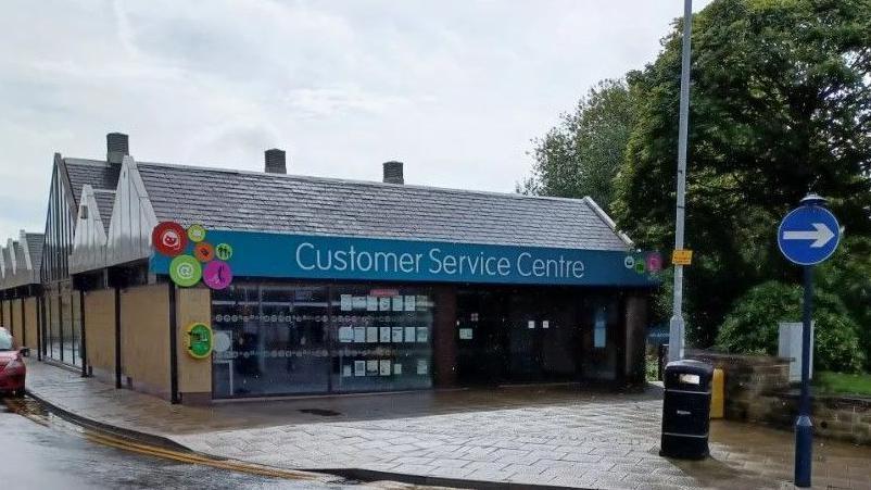 A single-story building with a shop front and a blue sign which reads Customer Service Centre. 