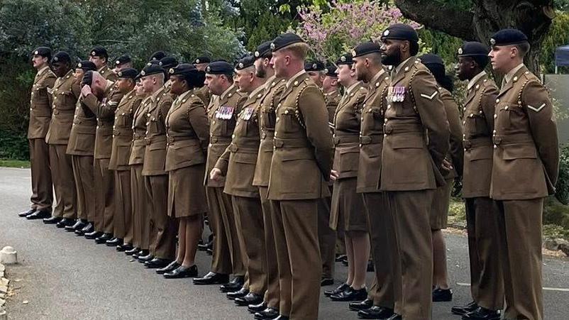A parade of about 40 military personnel in brown uniforms. They are standing in three rows.