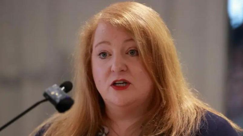 Naomi Long pictured beside a microphone. She has a navy top and the background is blurred.