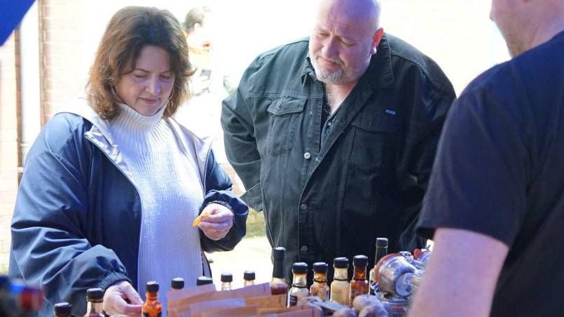 Ruth Jones seen visiting a market with Steve Speirs. She is wearing a blue rain jacket and a white turtle neck jumper and is looking at bottles of sauces at a stall.