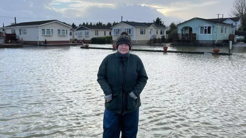 Sarah Dyke in waterproof coat and trousers standing in floodwaters in a caravan park