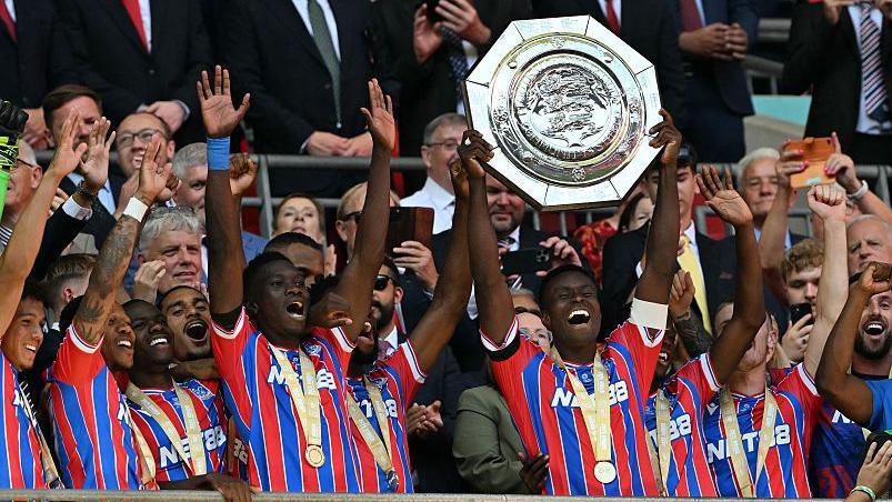 Marc Guehi lifting the Community Shield trophy with Crystal Palace players celebrating around him.