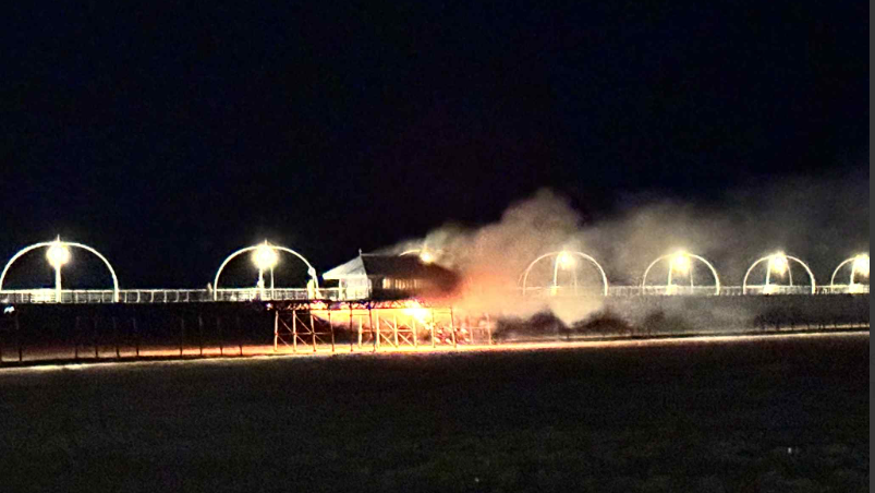 Smoke and fire billows from the pier surrounded by black sky