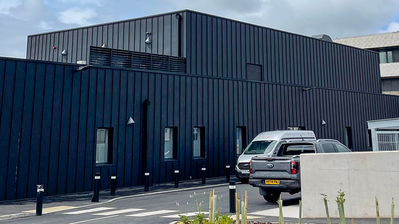The new Sulis Orthopaedic Centre at Sulis Hospital in Peasedown St John. The building looks quite blocky and dark and has a pedestrian crossing out the front with two cars parked outside.