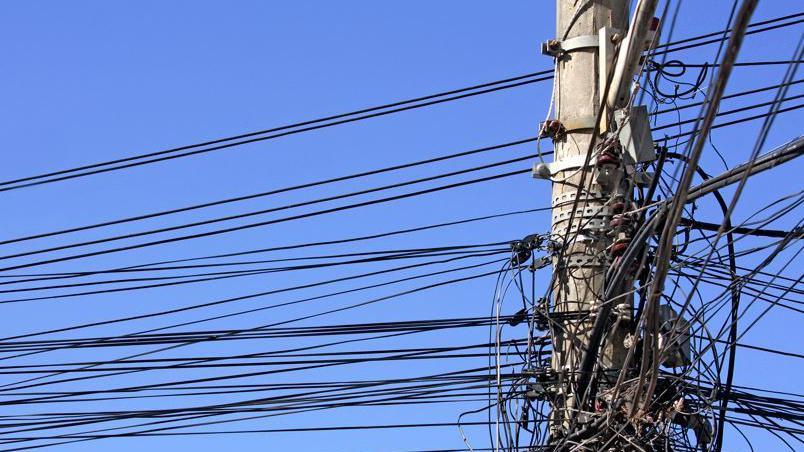 A wooden post with dozens of black power cables feeding out of it. The sky is blue in the background.