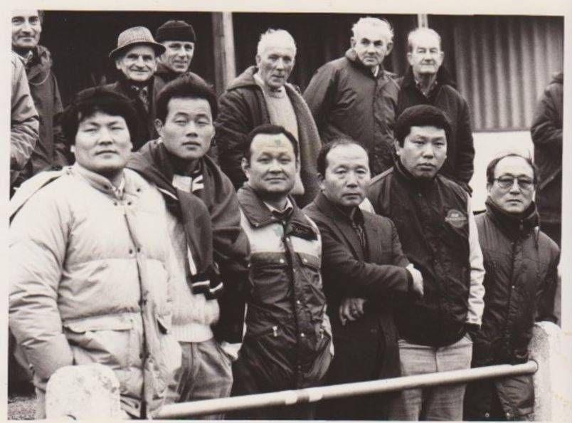 A black and white photo of several Korean men standing in a rugby stand in thick jackets.