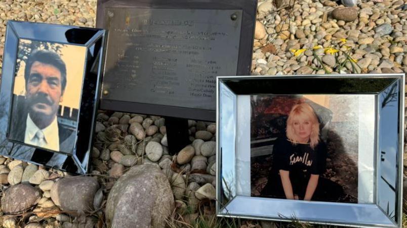 Silver-framed portraits of Vince Pettitt on the left and his daughter, Joceyln, on the right, are close to a memorial plaque with local victims' names on it. They are all on a bed of decorative stones.