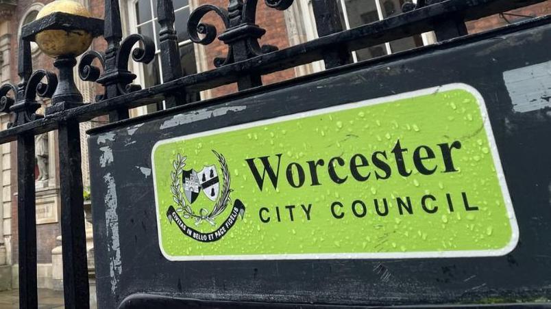 A sign at Worcester City Hall for the city council. The green sign has raindrops on it and is attached to black metal railings.