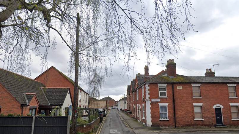 A residential street with red brick and pebble-dash houses. on either side. The branches of a tree are hanging over the top of the image