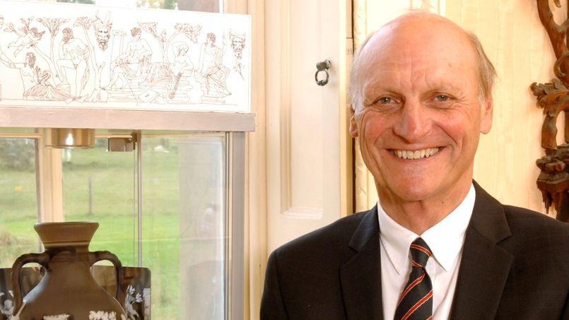 Graham Knowles at home pictured smiling at the camera. He is wearing a suit and tie. There is a vase and window behind him. 