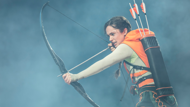 Mia Carragher as Katniss holding a bow and arrow 
