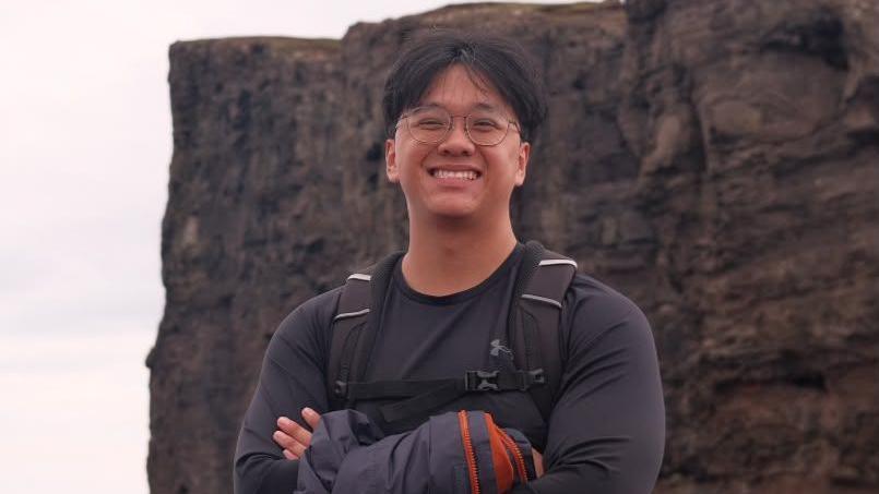 Shyan Lim smiling for a picture with his arms crossed during a hike near a cliff
