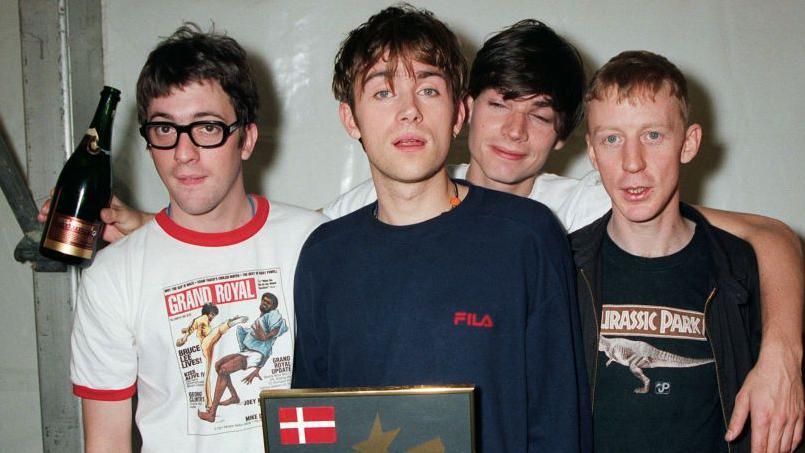 A picture of Blur in 1995 with Alex James with his arms round the other members