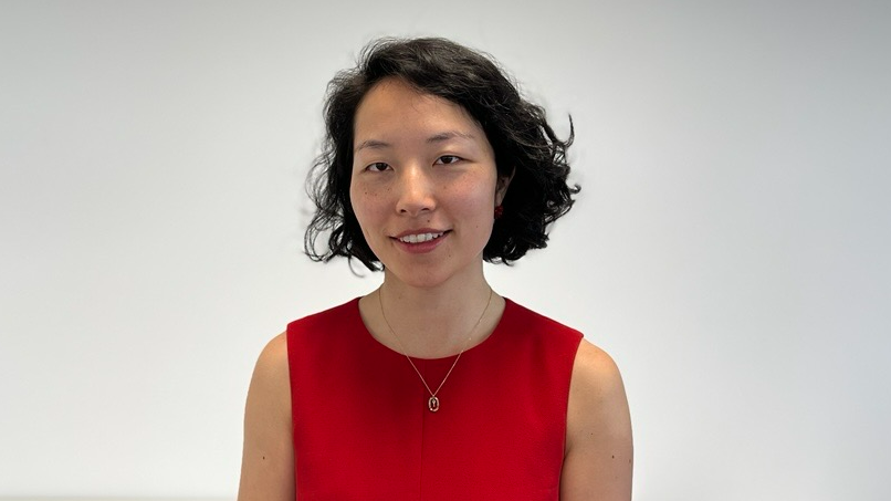 Yuan Yang, who has black hair and is wearing a red dress and golden necklace, in front of a grey background.