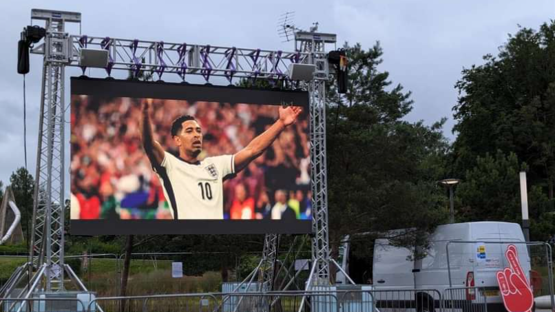 A large outdoor TV screen showing an England match