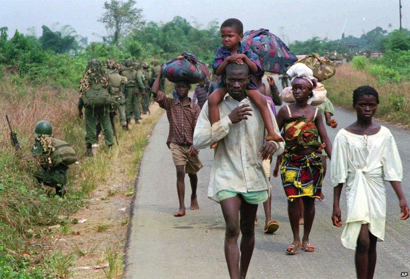 People fleeing the fighting in northwestern Liberia make their way down a road some seven miles from the capital of Liberia, 1995. Soldiers of the West African Peacekeeping Force (ECOMOG), walk in the opposite direction on the side of the road.