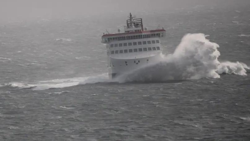 The Manxman, a large white ferry, being hit by a large wave, on a foggy day in a grey looking Irish Sea.