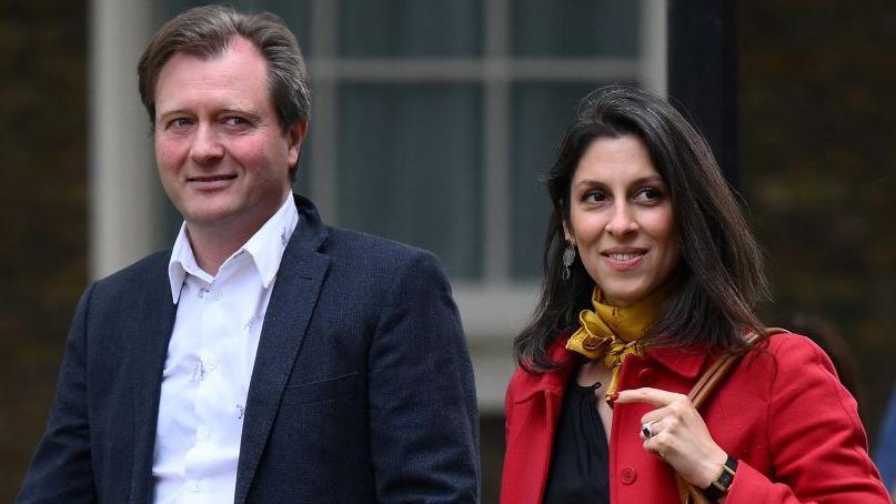 Richard Ratcliffe, wearing a white shirt and dark jacket, with Nazanin Zaghari-Ratcliffe, wearing a red coat with a yellow neckerchief, pictured outside as they walk next to each other in Downing Street