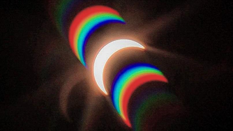 A view of the sun, partially covered, being reflected against blue, green and red wavelengths of light in the same semi-circle shape.