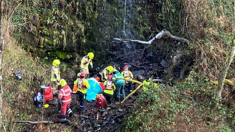 Llun o Suzie yn cael ei hachub ar waelod llethr serth ac aelodau o'r tim achub mynydd yn ei helpu.