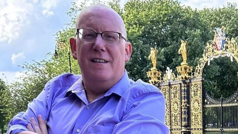 Councillor Graham Gowland stood by the golden gates in Warrington