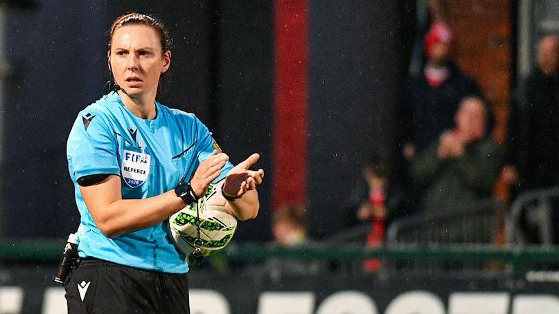 Referee Louise Thompson, who is wearing a vlue and black referee unfirom, joins in with a planned applause on the 30th minute to end violence against women and girls during today’s league fixture at Solitude, Belfast.