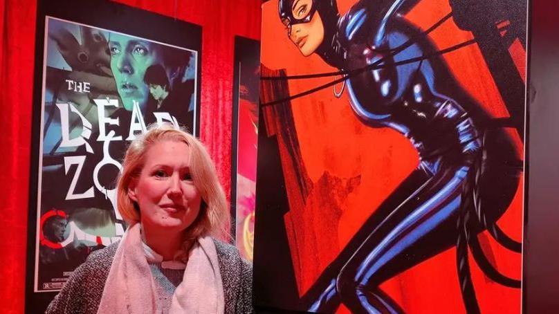 Lisa Wood, who has shoulder-length blonde hair, stood next to a poster of Catwoman.