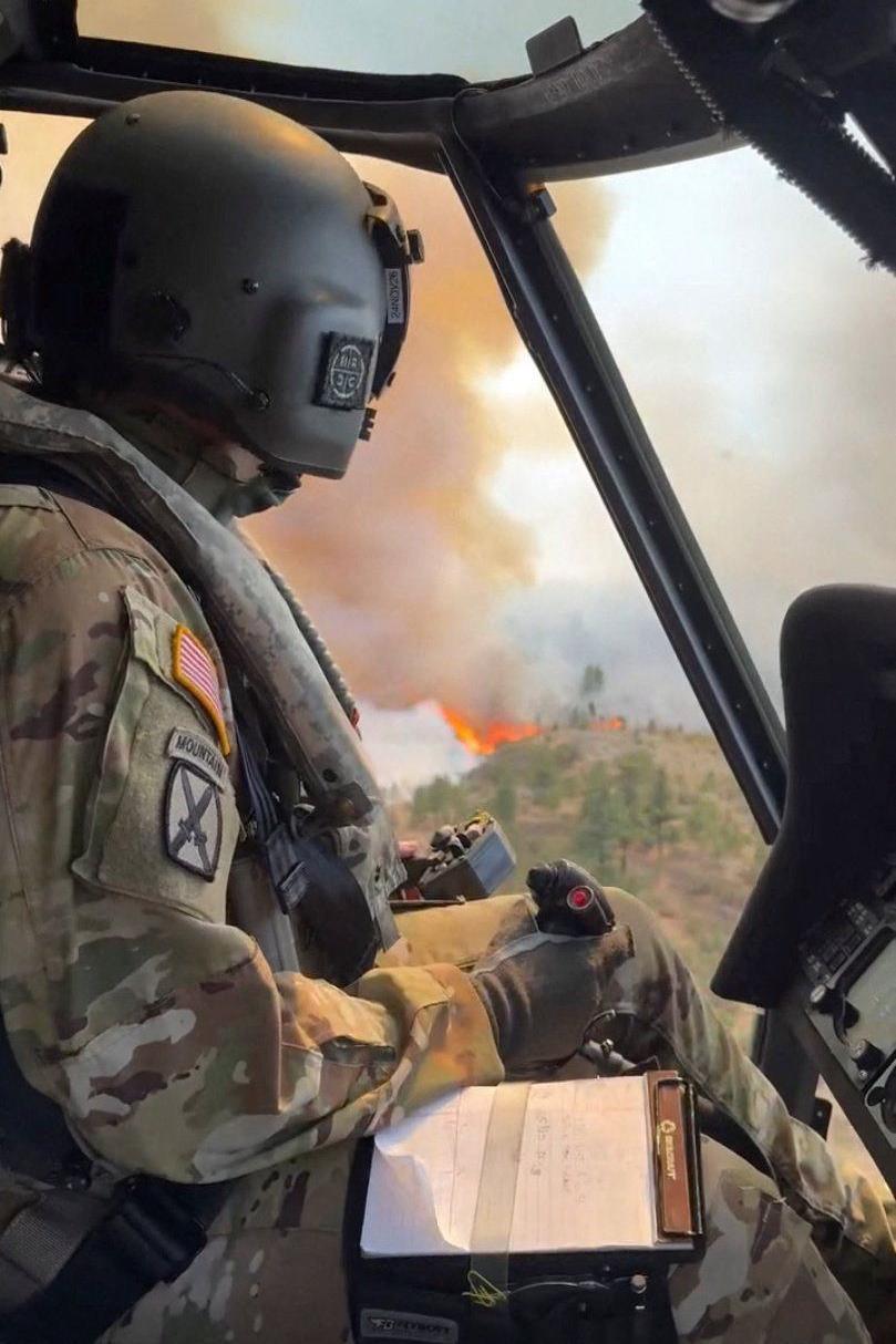 An image taken from a video shows a National Guard member in a helicopter - in the background outside are flames and smoke billowing
