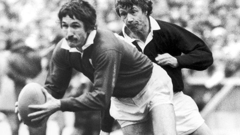 Gerald Davies on Murrayfield rugby pitch in 1975. The picture is in black and white and shows Davies running while carrying a rugby ball, and another player close behind him