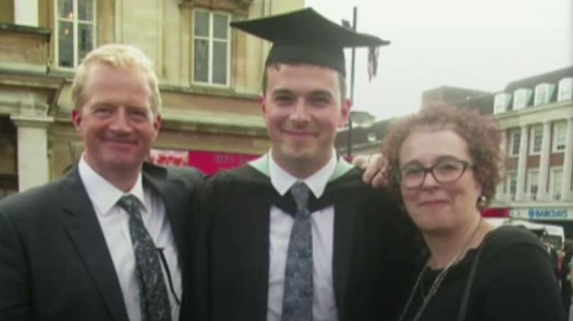 Charles and Liz Ritchie dressed smartly, standing either side of their son Jack at his graduation. Jack wears graduation robes and a mortar board.