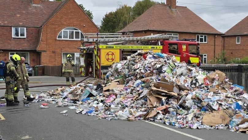 Pile of rubbish with firefighters around it