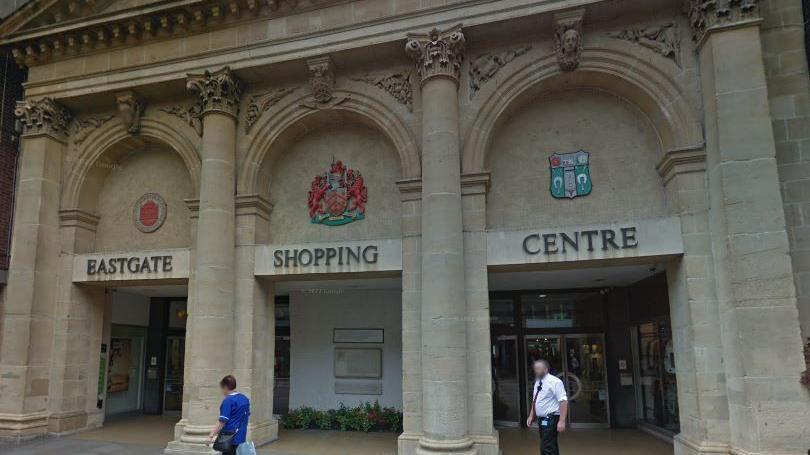 Entrance to Eastgate Shopping Centre in Gloucester, with two people walking past it