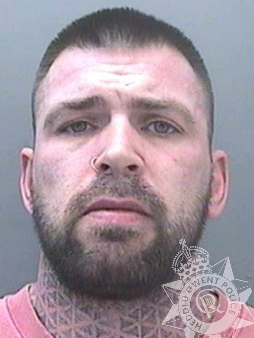 A police mugshot of a white hit-and-run driver with a beard and short brown hair with a tattoo on his neck