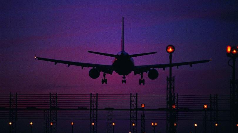 A silhouette of a plane taking off from a runaway, seen against a deep purple sky