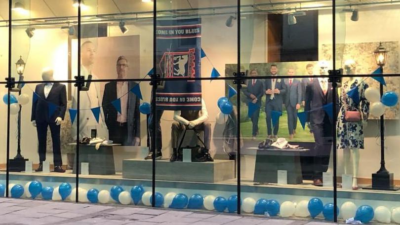 Store window showing Ipswich town flag and blue and white balloons