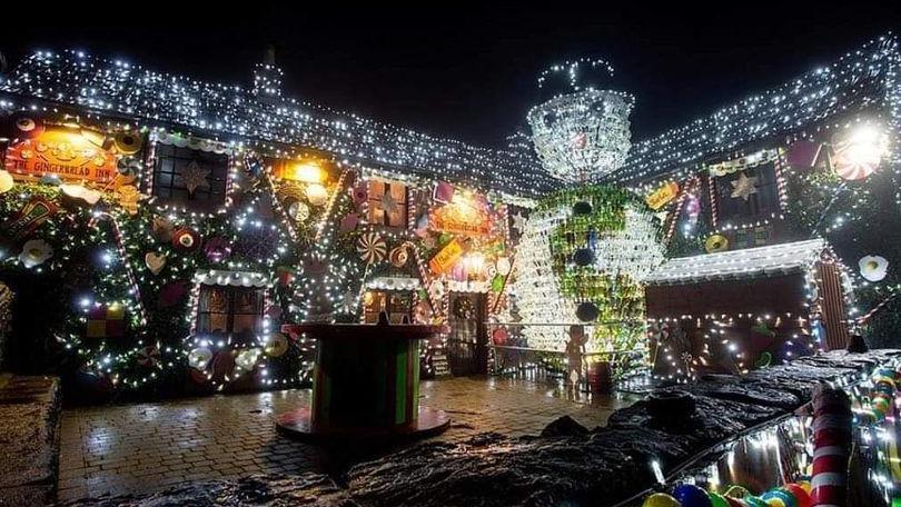 A large illuminated snowman wearing a green scarf sits in front of a pub garden, with the pub itself covered in Christmas lights and decorations.