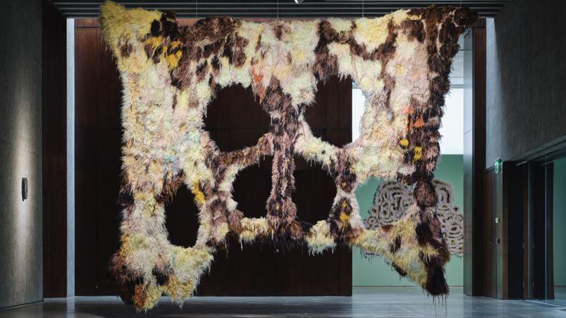 A textile work by Caroline Achaintre. It is a hanging piece with a number of large holes in it